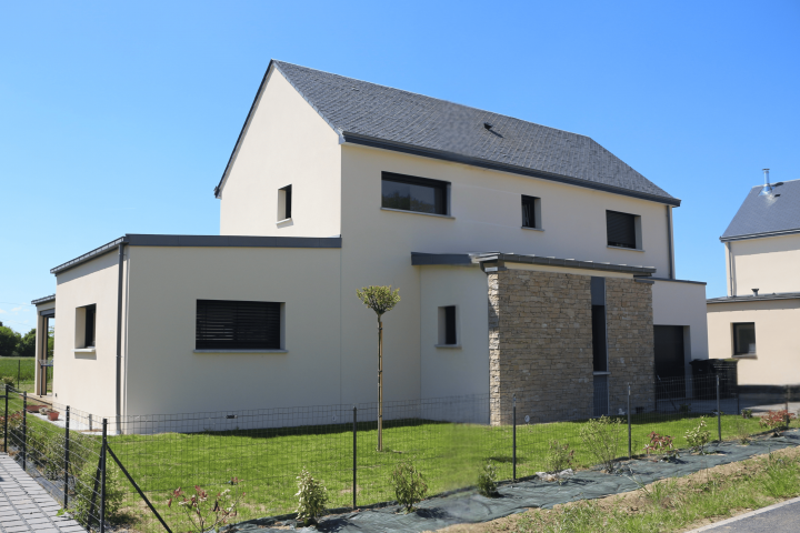 Maison contemporaine à étage avec toit en double pente, façade en enduit clair et parement pierre, menuiseries noires et jardin paysager